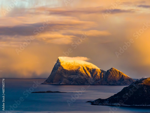 snowy mountain in the sea in rays of orange touching the clouds with peak
