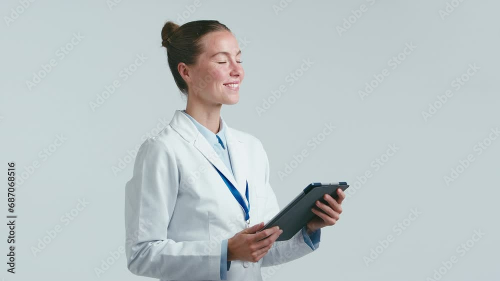Studio portrait of female doctor wearing white coat holding digital tablet against white background - shot in slow motion Studio portrait of female doctor wearing white coat holding digital tablet against white background - shot in slow motion