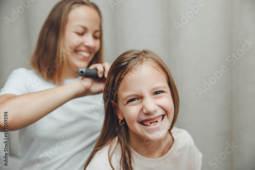 a little dark-haired girl looks into the camera and smiles while her mother combs her daughter's hair. hair care