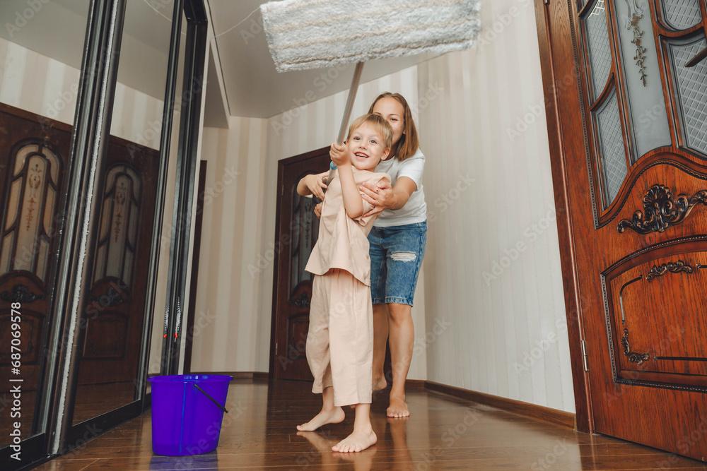 Little helper. Adorable baby helps his mother wash the floor, the child takes a rag from a bucket, together they clean the living room Little helper. Adorable baby helps his mother wash the floor, the child takes a rag from a bucket, together they clean the living room