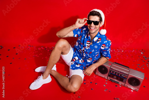 Full length photo of nice young male cool party boom box sunglass dressed santa claus print x-mas garment isolated on red color background