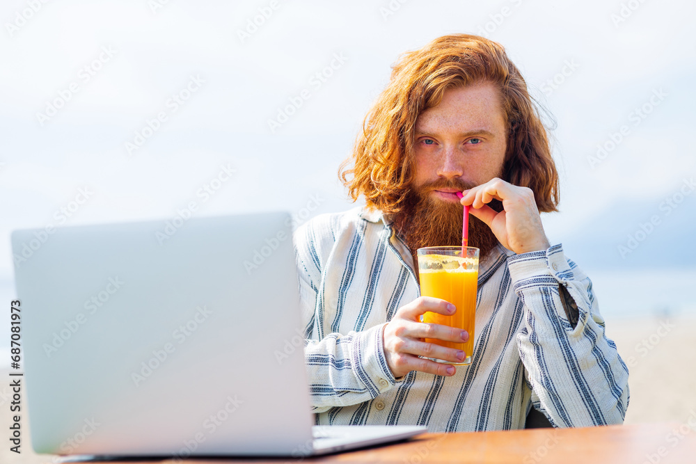 young redhaired ginger bearded man working outdoors in sea cafe with laptop an summer day young redhaired ginger bearded man working outdoors in sea cafe with laptop an summer day