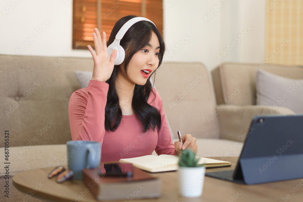 Young businesswoman greeting with colleague and writing notes in paper while talking on video call Young businesswoman greeting with colleague and writing notes in paper while talking on video call