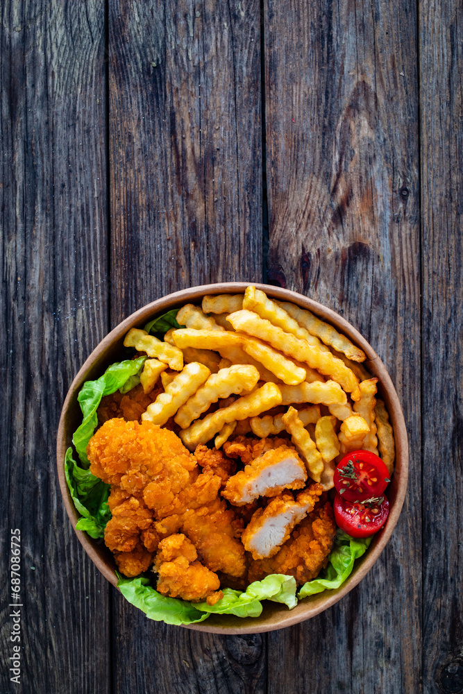 Fried breaded chicken nuggets served with French fries and vegetables on wooden table
Fried breaded chicken nuggets served with French fries and vegetables on wooden table