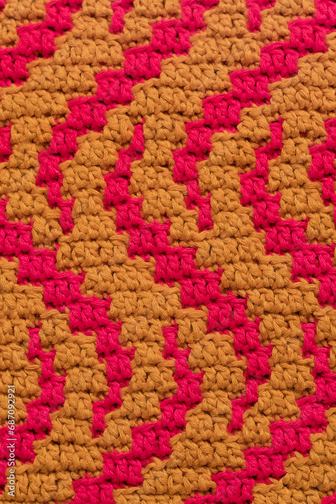 Yellow pink crochet mosaic fabric with wavy pattern close up. Knitted background.
