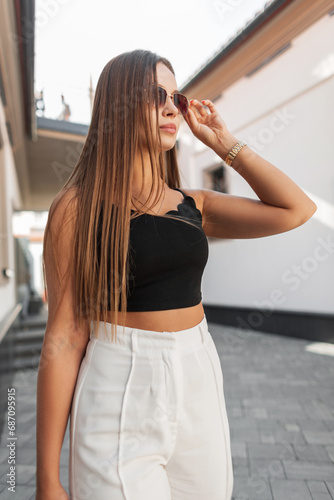 Stylish beautiful woman in fashion summer clothes walks in the city and adjusts her sunglasses. Pretty urban girl © alones