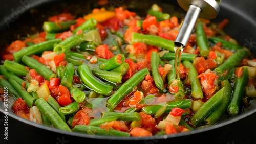 Pouring oil for frying vegetables in pan. Green beans, tomatoes, bell peppers ready for cooking