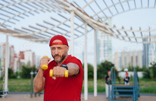 A middle-aged man in sports clothes trains outdoors with dumbbells and meditates boxing punches. Sports fitness active healthy lifestyle.