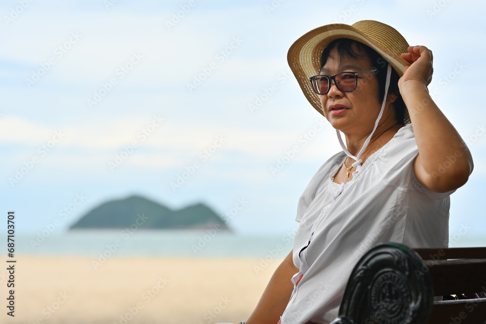 A Happy old woman in a hat sitting on a bench on the beach, Enjoy your retirement by the sea