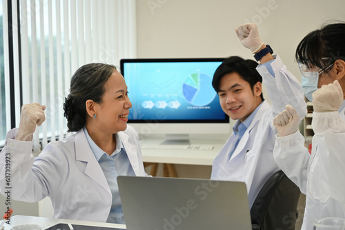 The Lab team working in the laboratory succeeds with their medical experiment, showing a happy and excited expression, raised hands, and a smile photo
