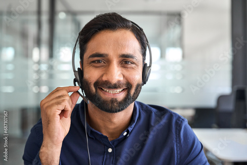Happy Indian man call center agent wearing headset in office. Smiling male contract service representative telemarketing operator looking to camera working in customer support. Headshot portrait. photo