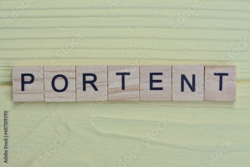 the word portent of gray small wooden letters lies on a yellow wooden table
