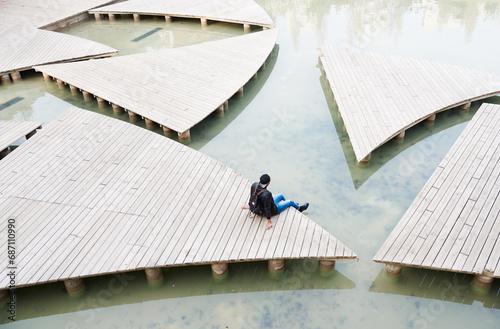 Man in cap with backpack sitting on platform. Young urban man resting sitting on the edge of an artificial lake in his city photo