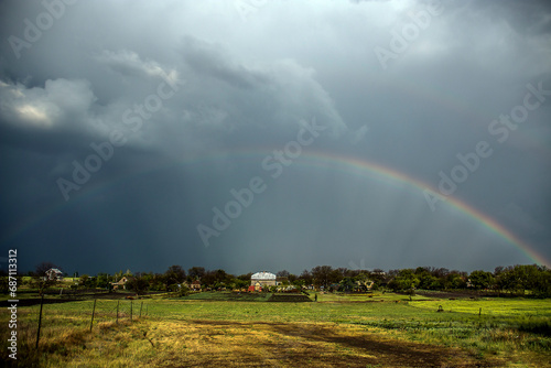 Multicolored rainbow in the sky during the rain in a cloudy cloudy sky over a field and a village 