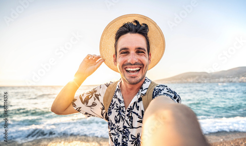 Happy handsome man taking selfie pic with cellphone outside - Male tourist enjoying summer vacation at beach holiday - Travel life style concept with smiling guy laughing at camera photo