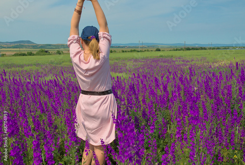 Fototapeta Naklejka Na Ścianę i Meble -  A girl in spring flowers in a field in nature poses for a blog. Purple field of Delphínium flowers