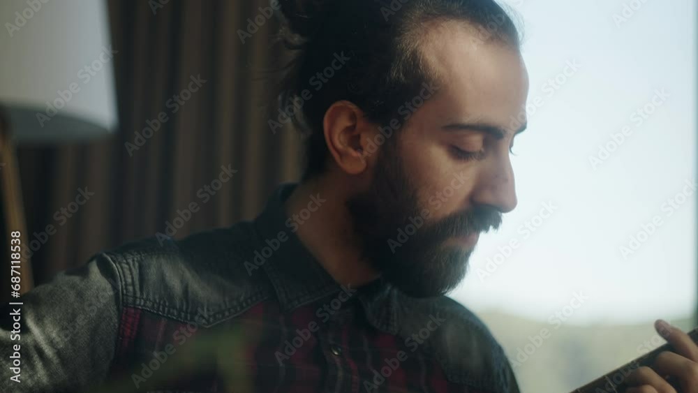 Bearded young adult man playing acoustic guitar while sitting on sofa at home. Camera moving down and up Bearded young adult man playing acoustic guitar while sitting on sofa at home. Camera moving down and up