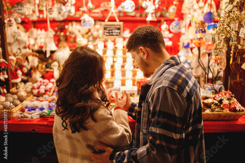 Young stylish couple in love in checkered coats choosing the Christmas toys at Christmas Verona market