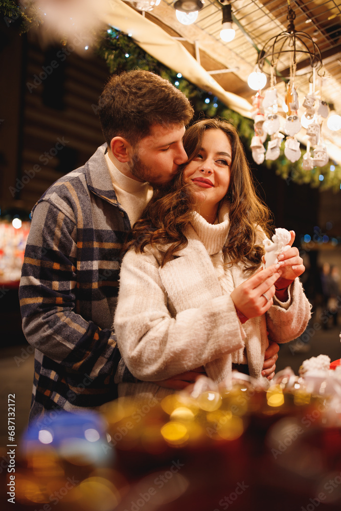 Young stylish couple in love in checkered coats choosing the Christmas toys at Christmas Verona market Young stylish couple in love in checkered coats choosing the Christmas toys at Christmas Verona market