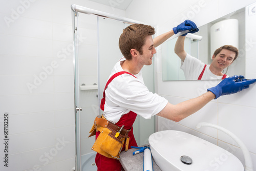 The worker installs the mirror in the bathroom