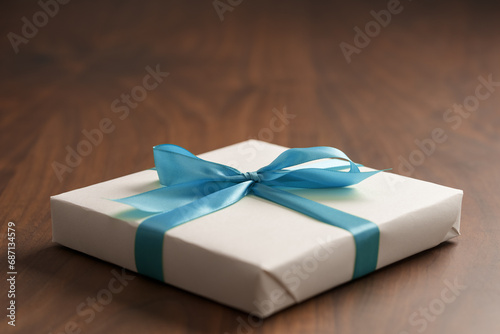 White paper gift box with blue ribbon on walnut wood table with copy space