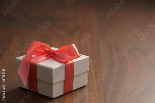White paper gift box with rose ribbon on walnut wood table with copy space