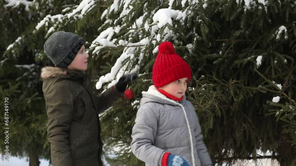 Cute little girl in red cap and teen kid boy decorate a Christmas tree snowy winter outside. Cute little girl in red cap and teen kid boy decorate a Christmas tree snowy winter outside.