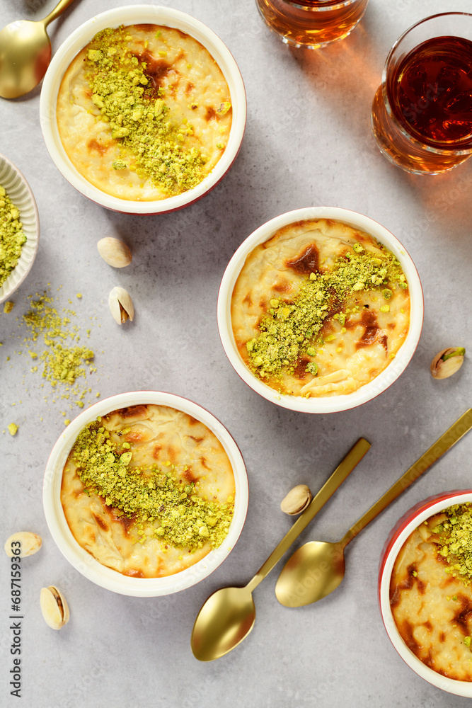 Baked rice pudding- traditional turkish milk dessert, served with pistachio nuts and cup of black tea. top view Baked rice pudding- traditional turkish milk dessert, served with pistachio nuts and cup of black tea. top view