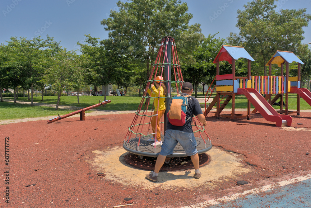 Εκτύπωση καμβά A child on a children's carousel is spun by his father on a playground in a park on a clear sunny day