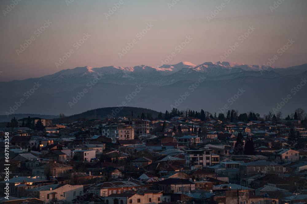 Landscape of a small old town against the backdrop of snow-capped high-altitude mountains during sunset