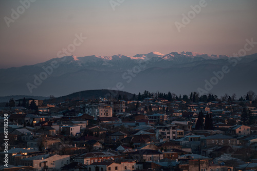 Landscape of a small old town against the backdrop of snow-capped high-altitude mountains during sunset