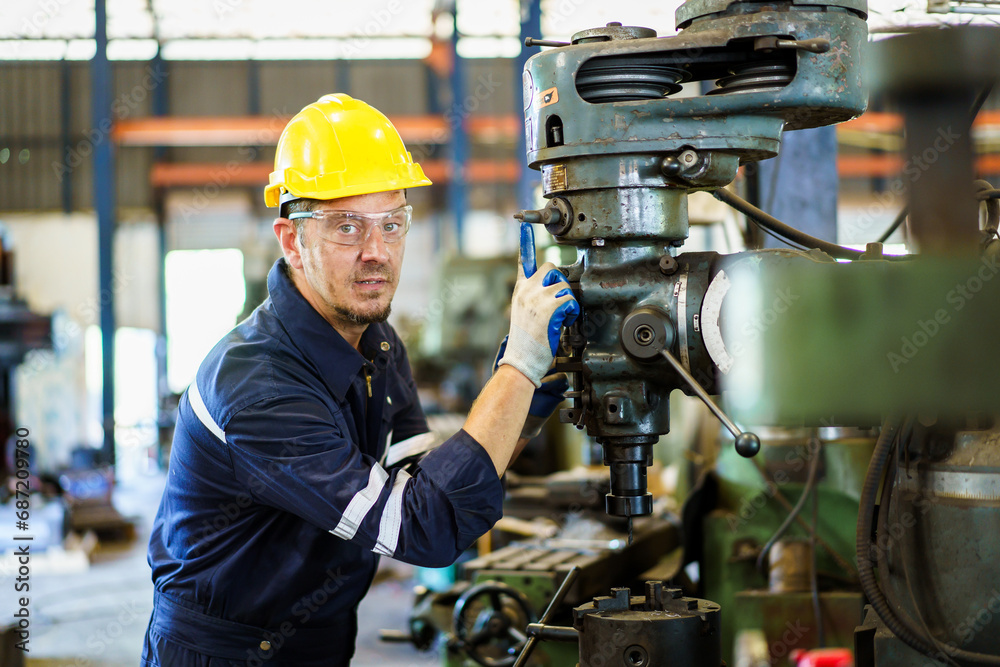 Professional caucasian white ethnicity male technician operating the heavy duty machine in the lathing factory. Technician in safety and helmet suit controlling a machine in factory. Professional caucasian white ethnicity male technician operating the heavy duty machine in the lathing factory. Technician in safety and helmet suit controlling a machine in factory.