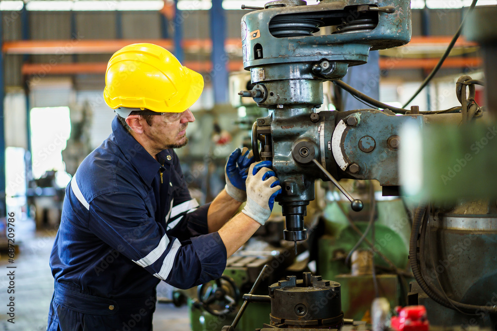 Professional caucasian white ethnicity male technician operating the heavy duty machine in the lathing factory. Technician in safety and helmet suit controlling a machine in factory. Professional caucasian white ethnicity male technician operating the heavy duty machine in the lathing factory. Technician in safety and helmet suit controlling a machine in factory.