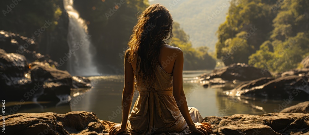 Yoga poses. a Woman sitting on a rock overlooking a waterfall view from a distance