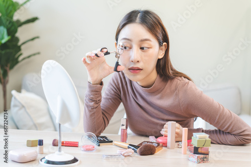 Beauty concept, beautiful asian young woman, girl makeup face by using an eyelash curler to curl my eyelashes before apply mascara, looking at the mirror at home. Female with natural fashion style.