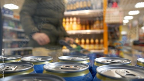 A man with a shopping trolley opens the fridge door and takes three cans of beer photo