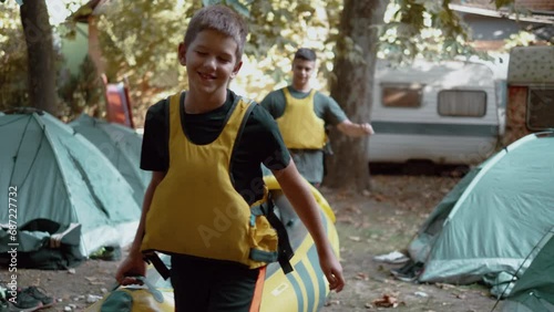 Teenagers in a life jacket at camp carry rubber kayaks ready to ride photo