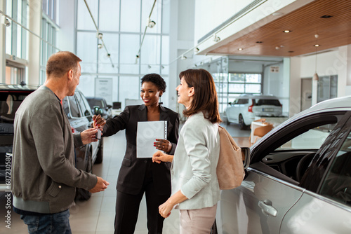 Couple signing paperwork to purchase a new car at dealership with saleswoman photo