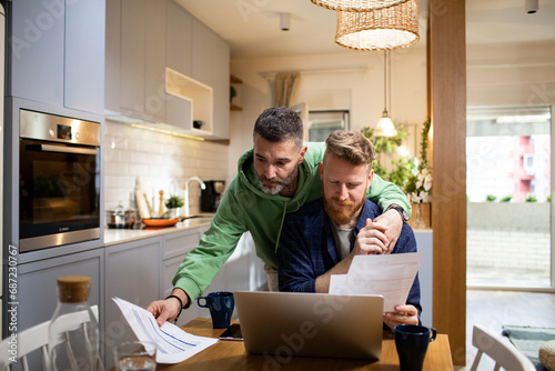 Same-sex male couple reviewing documents together, financial planning at home photo