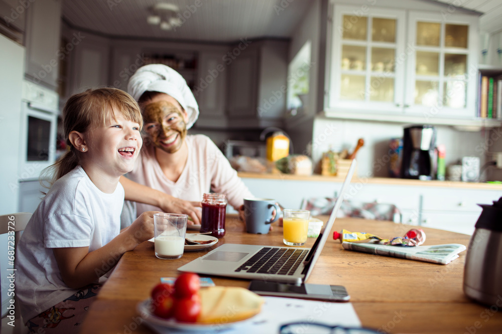 Mother and daughter using laptop during breakfast in the kitchen Mother and daughter using laptop during breakfast in the kitchen