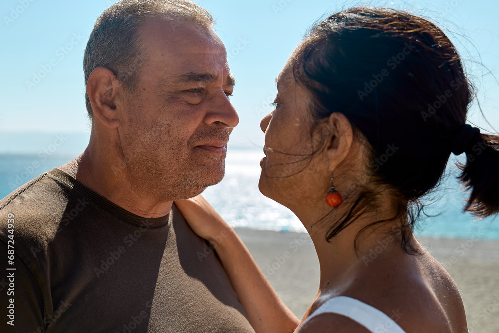 Closeup portrait of happy middle aged couple enjoying romantic moment on the beach. Mature man and woman looking into each other's eyes, touching their foreheads together before kiss near seaside. Closeup portrait of happy middle aged couple enjoying romantic moment on the beach. Mature man and woman looking into each other's eyes, touching their foreheads together before kiss near seaside.