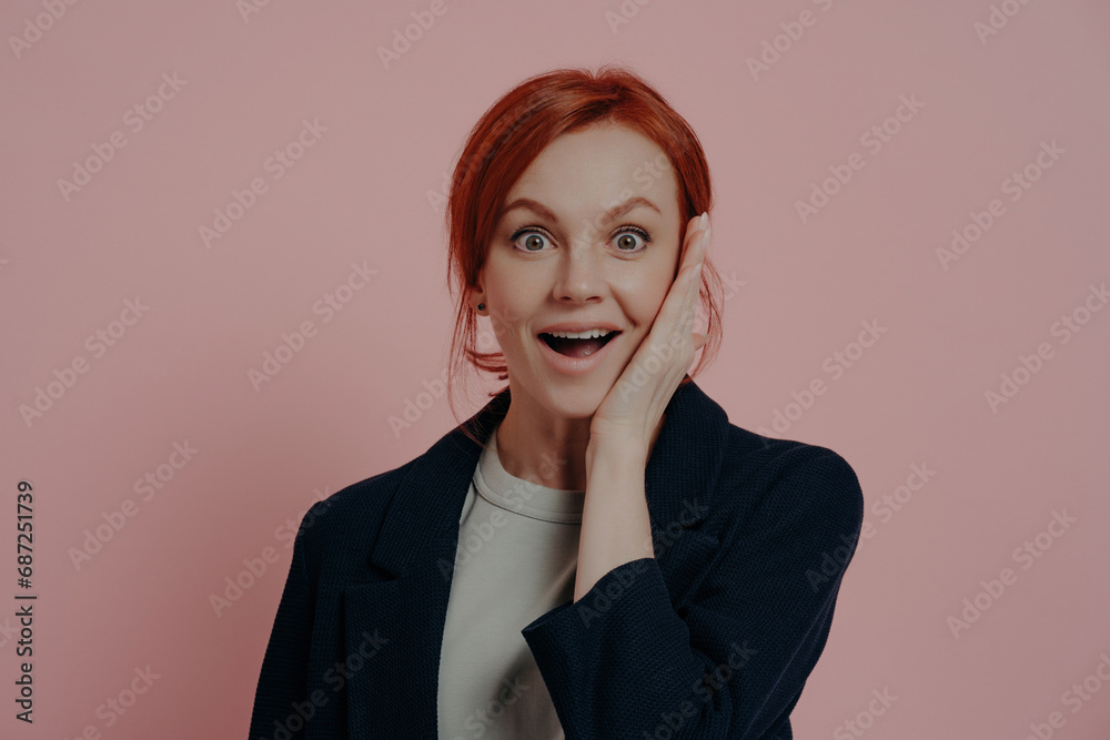 Surprised redhead woman with hand on cheek, wide-eyed in amazement, wearing a navy blazer Surprised redhead woman with hand on cheek, wide-eyed in amazement, wearing a navy blazer