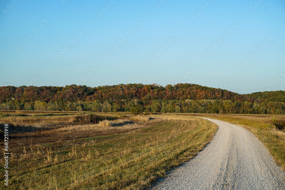 Fall leaves on trees up on bluff overlooking field with gravel road