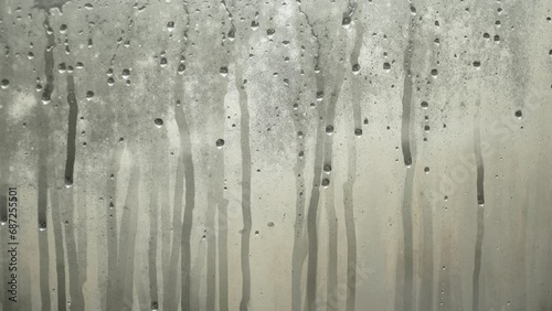 Background video of water drops flowing down foggy cold window during day. Condensation and high humidity in winter on non-energy efficient glass. Melting during change of season.