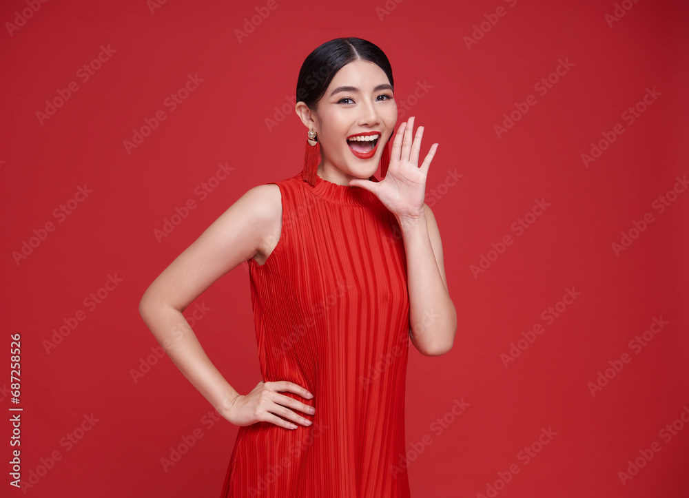 Happy Asian woman wearing red dress with open mouths raising hands screaming announcement isolated on red copy space background. Happy Asian woman wearing red dress with open mouths raising hands screaming announcement isolated on red copy space background.