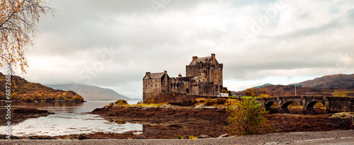 A majestic castle stands tall on a secluded island, surrounded by the tranquil waters of a glistening lake, as the cloudy autumn sky frames the rugged mountains in the distance, with its tower reachi photo