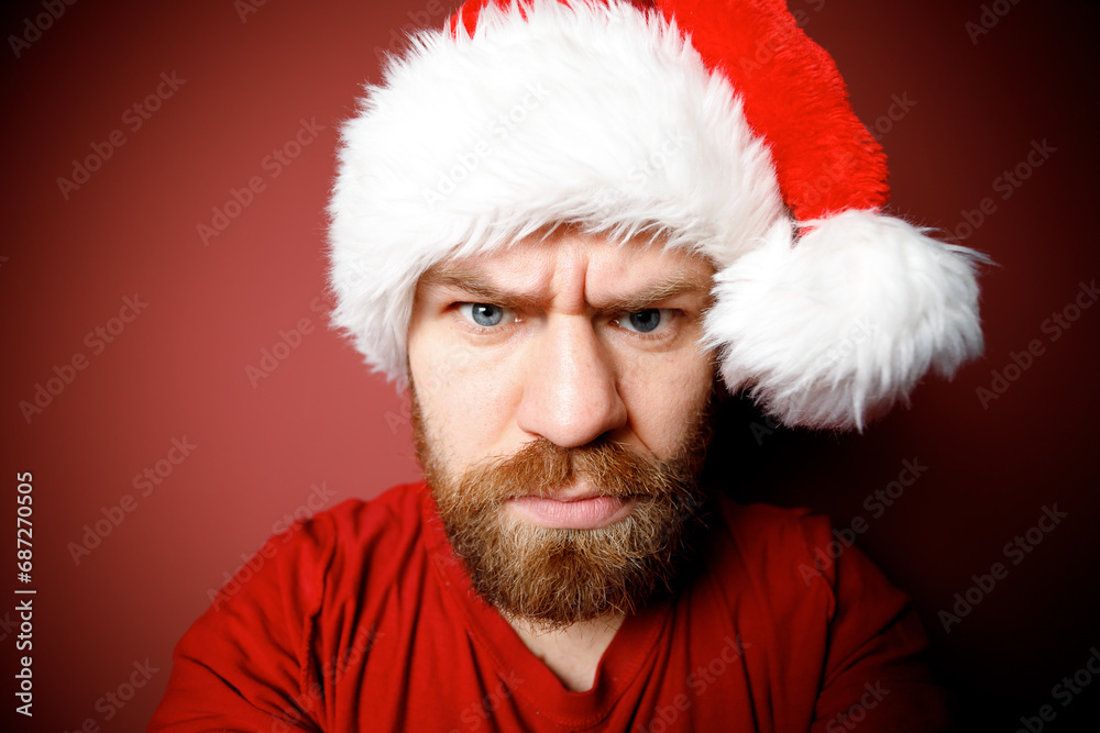 Naklejka premium Close Portrait of bearded Santa Claus in red hat, white beard with pensive emotion on red background