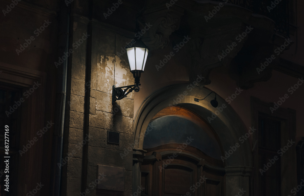 An old wall lamp shines with a warm light in the center of night Lviv. The concept of the evening city, the historical part.