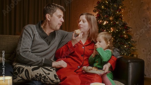 Happy family watching a movie on Christmas eve with child and eating gingerbread cookies, entertainment on New Year's eve for a family with a toddler.