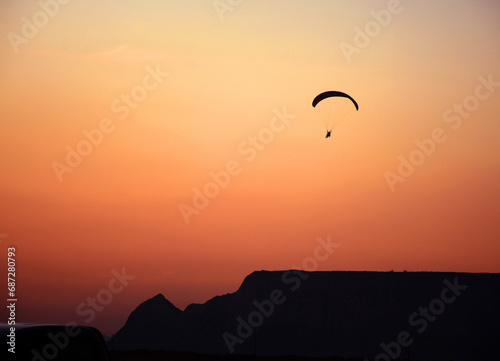 Paraglide sport silhouette over mountain of Naz island in sky with orange sunset.